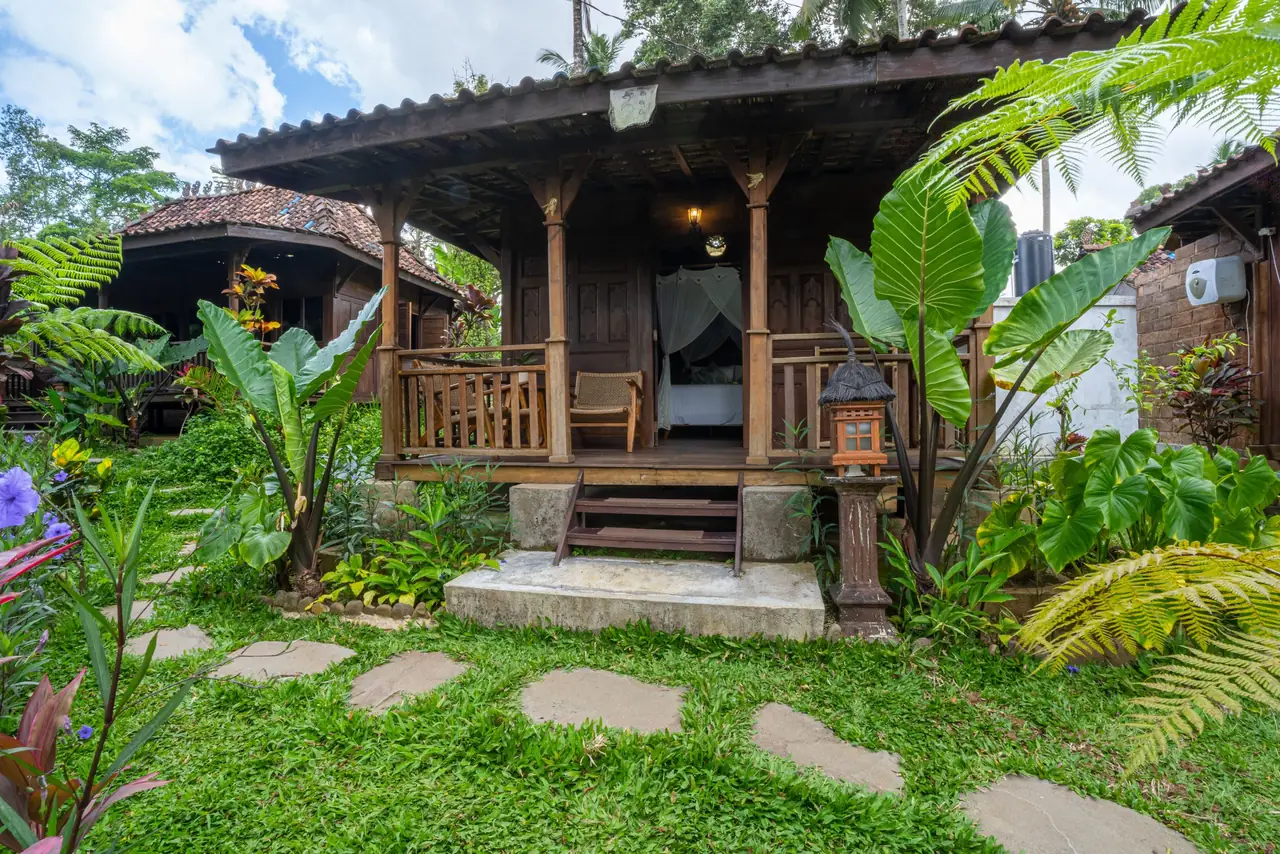 The wooden Joglo cottage in its tropical garden, with a stepping-stone path to the terrace